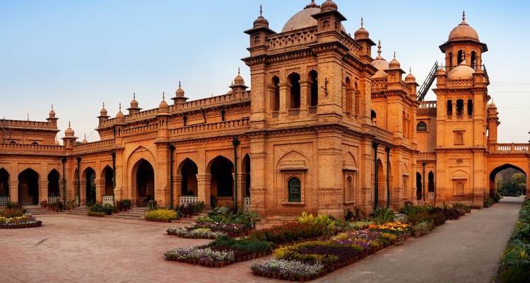 Historical building with arches and a garden at sunset.