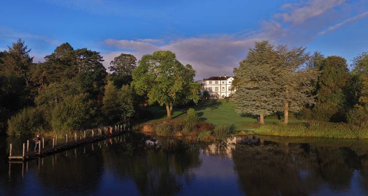 A classic house surrounded by lush trees seen from across a lake.