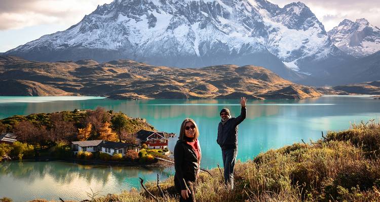 Two people standing on a hill with a pristine lake and snow-capped mountains in the background.