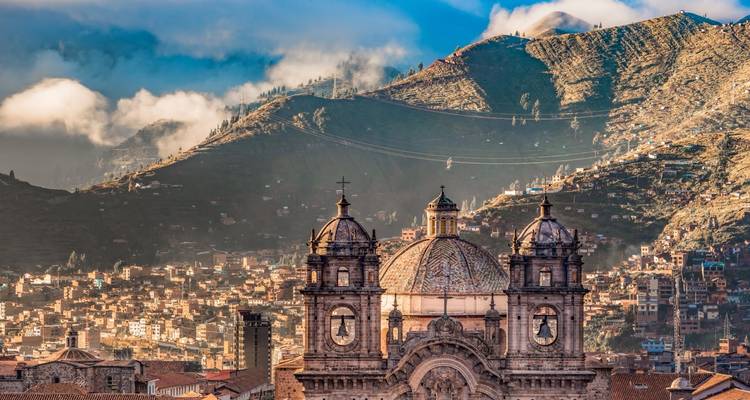 Historic cityscape with a cross-topped cathedral and mountainous backdrop.