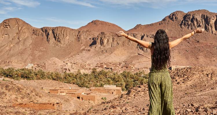 Femme aux bras levés regardant un paysage désertique avec des palmiers.