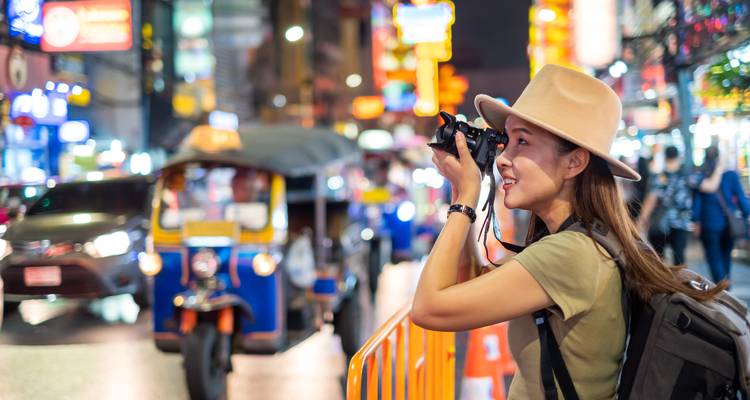 Frau fotografiert eine belebte Straße bei Nacht mit Tuk-Tuks.
