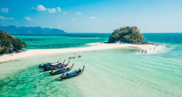 Strand mit Longtailbooten und Insel im Hintergrund.