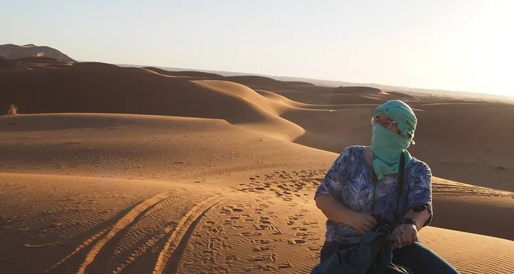 Person in traditional attire sitting on sand dunes.