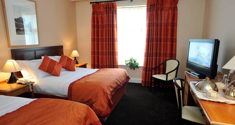 Interior of a hotel room with two beds, TV, and window with curtains.