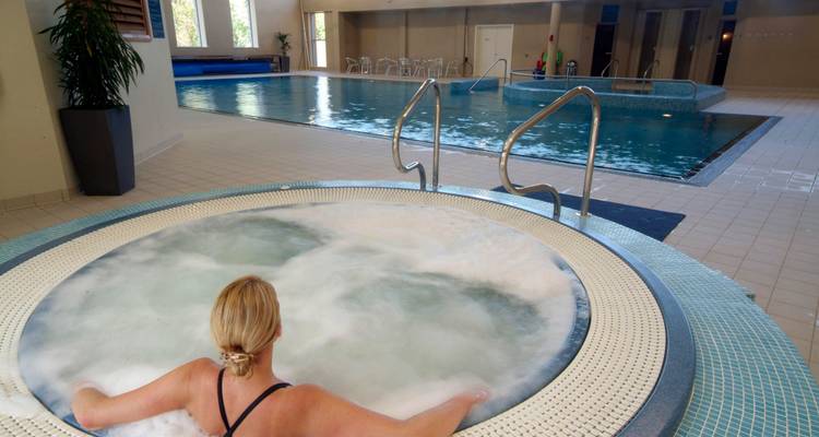 Indoor swimming pool area with a woman relaxing in a hot tub.