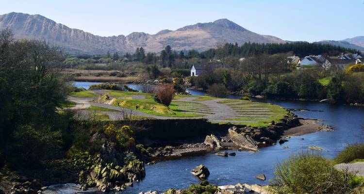 Riverside view with mountains and small houses in the distance.