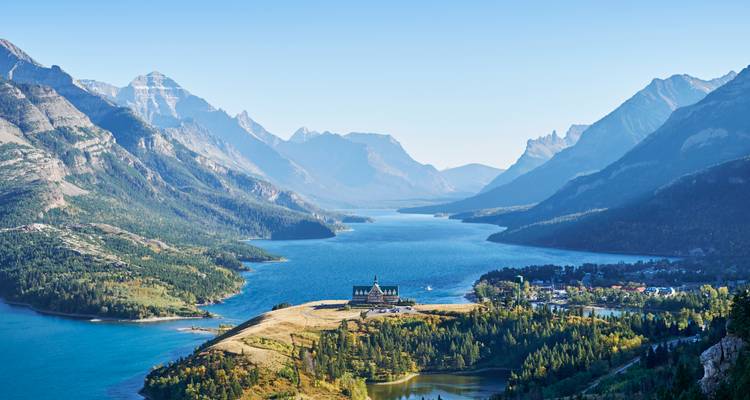 Vue panoramique d'un lac entouré de montagnes avec un grand bâtiment au bord du lac.