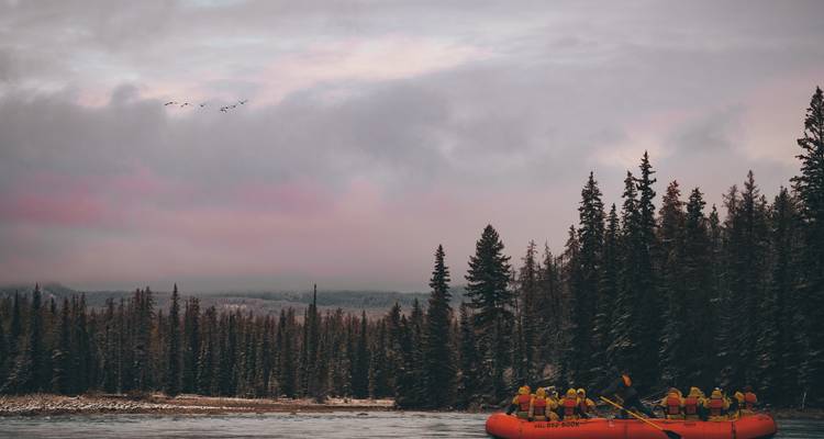 Groupe de personnes dans un radeau sur une rivière entourée de forêt.