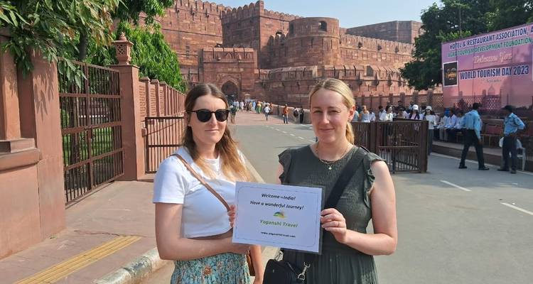 Twee vrouwen houden een bord vast voor een historisch rood fort.
