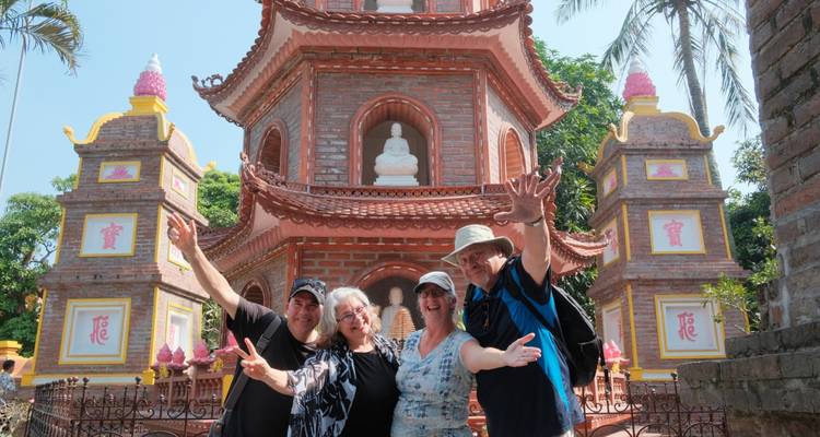 Groupe de quatre personnes posant joyeusement devant une pagode traditionnelle avec des statues.
