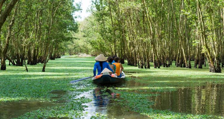 Des personnes dans un bateau naviguant sur une rivière verdoyante avec des arbres en surplomb.