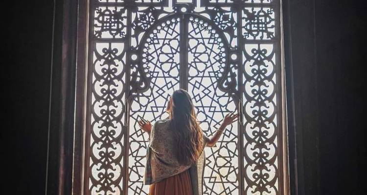 Persona parada frente a una ventana decorativa con diseños intrincados.