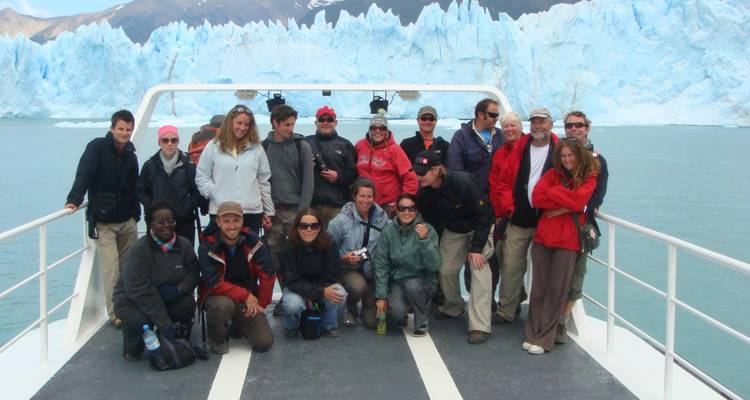 Group photo of tourists on a boat in front of a glacier.