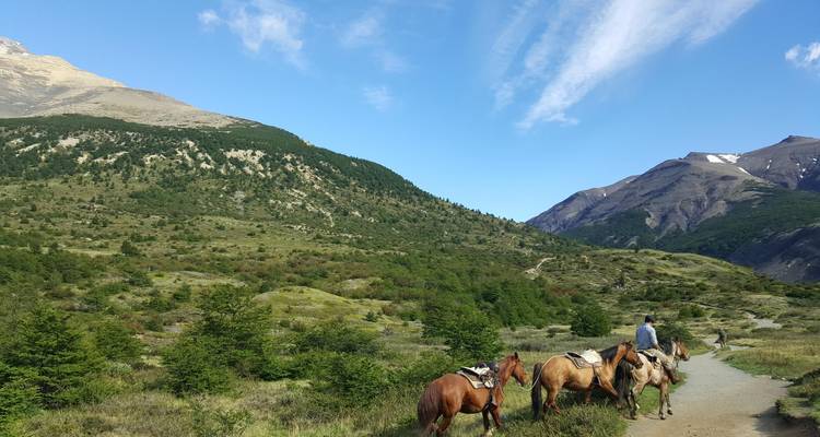 Horseback riders traversing green valley terrain with mountains in the background.