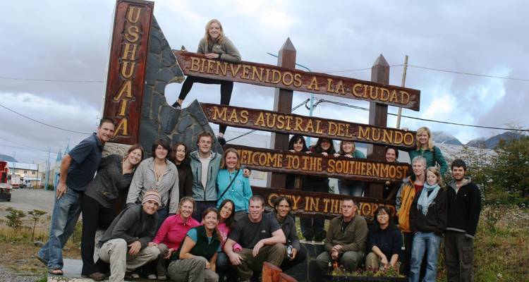 A group of tourists posing at a welcome sign in Ushuaia.