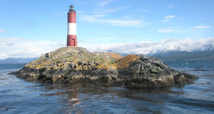 A lighthouse on a rocky islet with distant mountains.