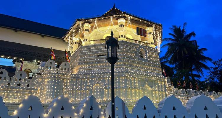 Une tour de temple bouddhiste blanche ornée de lumières scintillant de centaines de petites lumières contre un ciel du soir bleu profond.