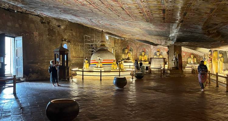 Les visiteurs photographient des statues gigantesques de Bouddha et un stupa sous un plafond de grotte aux couleurs vives.