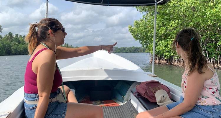 Deux femmes naviguent en bateau dans de calmes voies navigables de mangrove, pointant vers le rivage luxuriant.