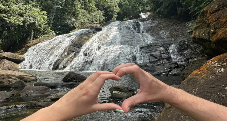 Les mains forment un coeur au premier plan encadrant une cascade de jungle.