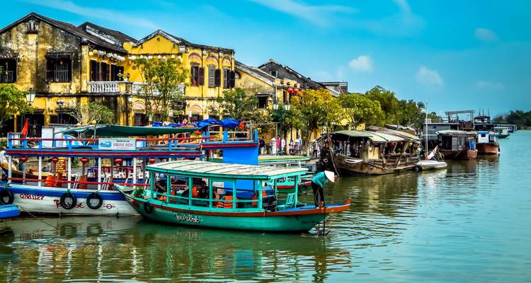 Bunte Boote auf einem Fluss mit traditionellen Gebäuden in Hoi An, Vietnam