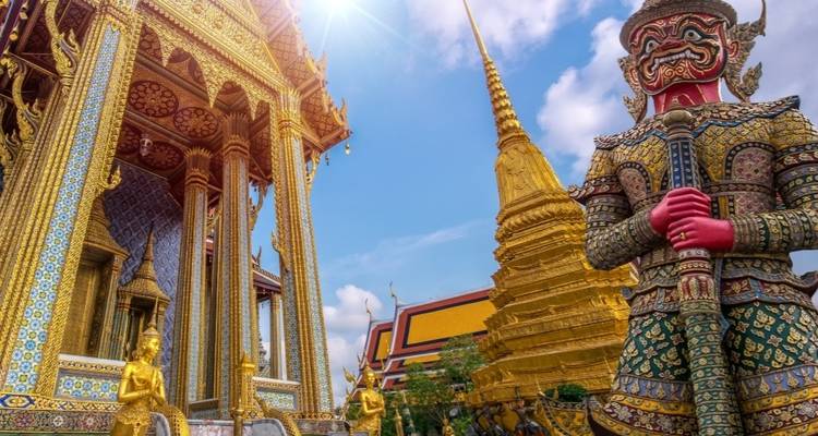 Close-up of ornate temple guard statue and golden stupa.