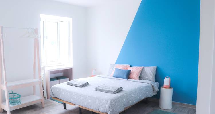 Helles Zimmerinterieur mit blauer Akzentwand und Bett.