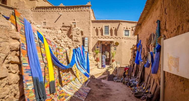 Des textiles colorés suspendus le long d'une rue étroite dans un cadre historique.