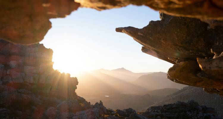 Lever de soleil sur les montagnes vu depuis une grotte rocheuse.