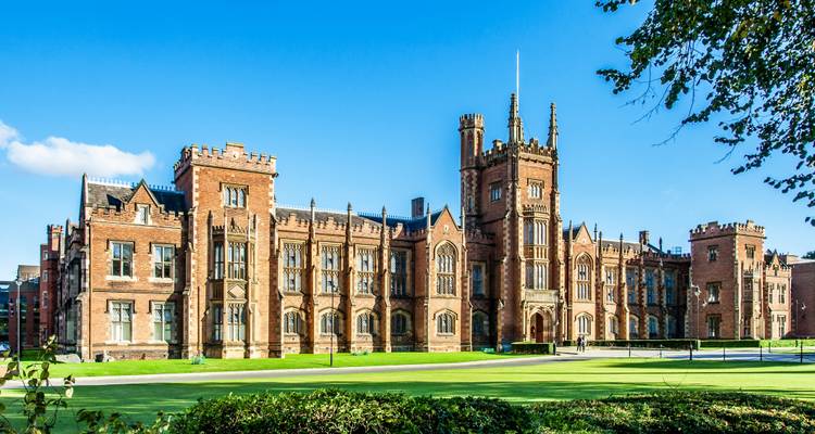 Élégant bâtiment en briques rouges de l'Université Queen's avec une pelouse verte bien entretenue sous un ciel bleu dégagé