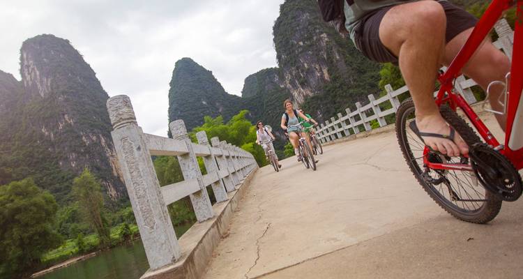 Los viajeros pedalean sobre un puente de piedra rodeado de dramáticos picos de karst.