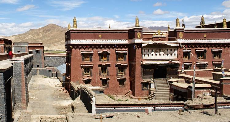 Historisch rood bakstenen Sakya Kloostercomplex tegen kale Himalaya heuvels onder blauwe luchten.