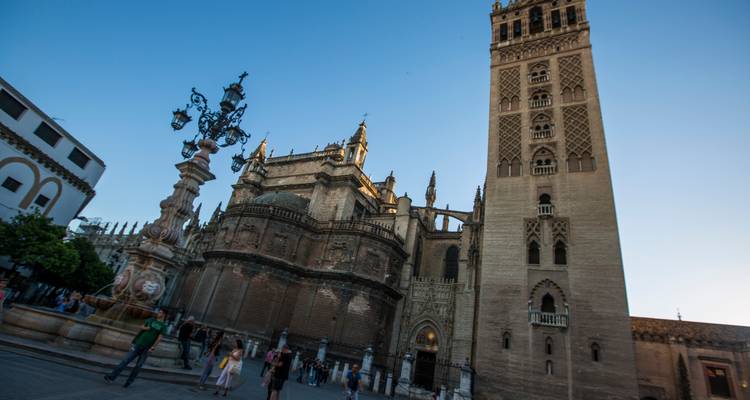 Vista amplia e inclinada de la Catedral de Sevilla y la torre Giralda con fuente en primer plano.