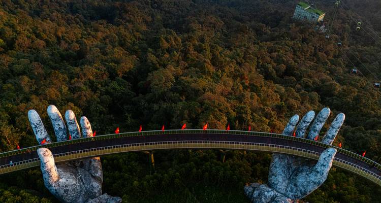 Die ikonische Goldene Brücke, von steinernen Händen gehalten, erstreckt sich bei Sonnenuntergang über den dichten vietnamesischen Wald.