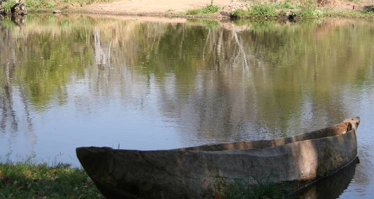 Traditional wooden dugout canoe resting in calm reflective waters of a small river or lake bank