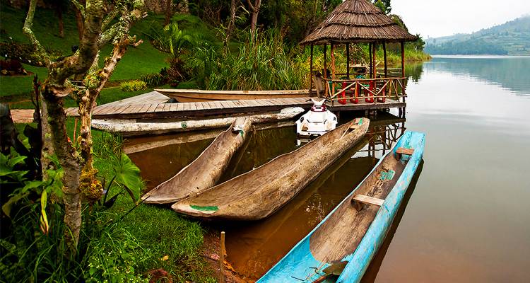 Canoas tradicionales excavadas en troncos y un pequeño mirador se encuentran junto a las aguas tranquilas del Lago Bunyonyi rodeadas de vegetación.