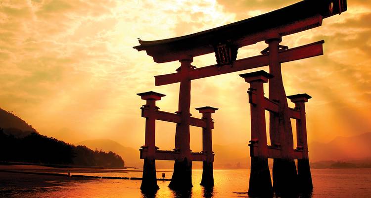El famoso torii del santuario Itsukushima recortado contra la luz dorada del atardecer sobre aguas tranquilas.