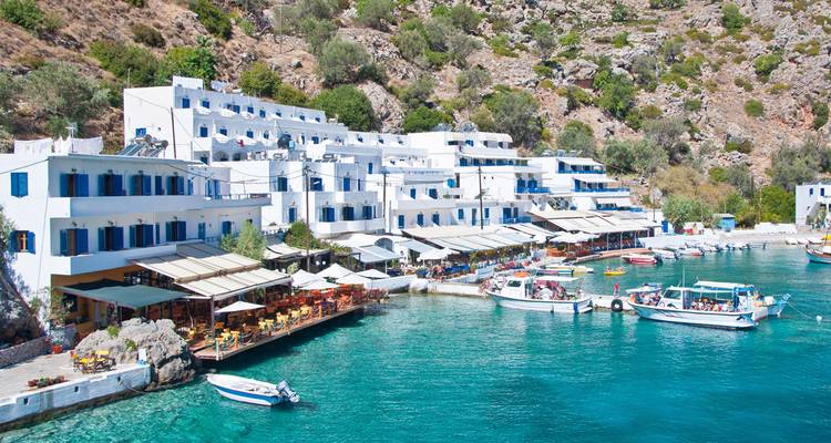 Village côtier blanchi à la chaux de Loutro avec des tavernes et des bateaux amarrés dans une eau turquoise.