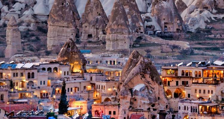 Las luces del atardecer brillan entre casas de piedra en cuevas y chimeneas de hada talladas en los acantilados de Capadocia.