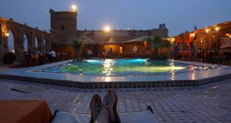 Scène de soirée d'une piscine de lodge du désert éclairée vue depuis une chaise longue avec des dîneurs en arrière-plan.