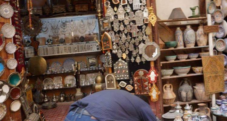 Intérieur flou d'un bazar de souvenirs rempli de bibelots en métal et de poterie avec un vendeur penché en avant.