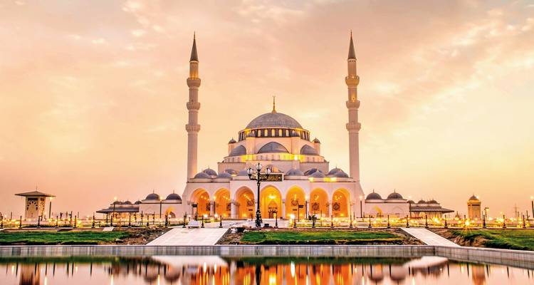 Elegante, illuminierte Moschee mit zwei Minaretten, die sich bei Sonnenuntergang in ruhigem Wasser spiegeln