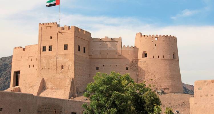 Historische Fujairah-Festung mit VAE-Flagge auf felsigem Hügel unter teilweise bewölktem Himmel