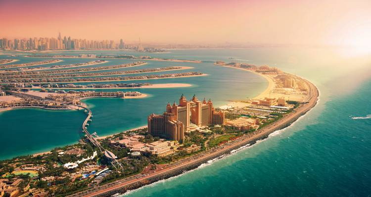 Luftaufnahme der Palm Jumeirah mit dem Atlantis-Resort und der sich ausbreitenden Küstenlinie in goldenem Sonnenuntergangslicht.