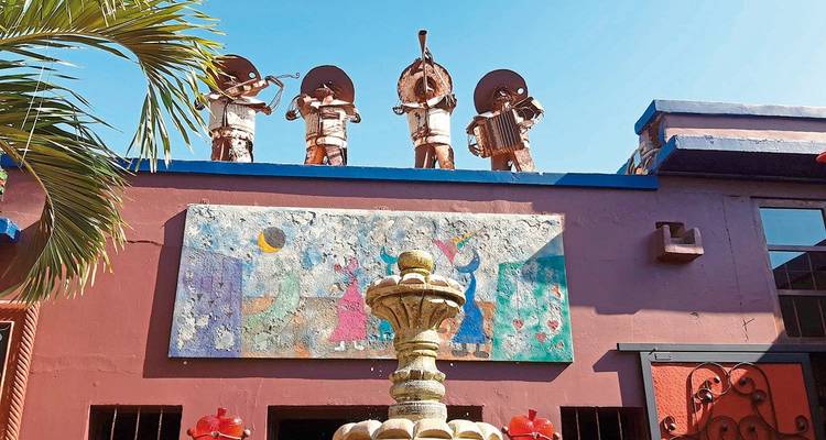 Statuen von Musikern an einem Gebäude mit einem bunten Wandgemälde und Brunnen.