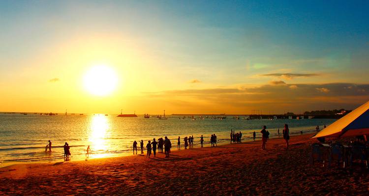 People enjoying the beach with a sunset over the ocean.