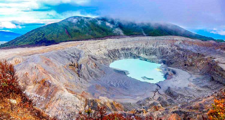 Cráter volcánico con lago turquesa rodeado de montañas.