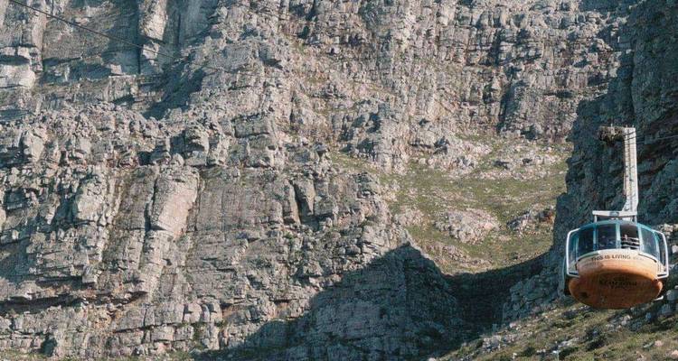 Un teleférico rotatorio asciende por los acantilados escarpados de Table Mountain bajo cielos azules despejados.