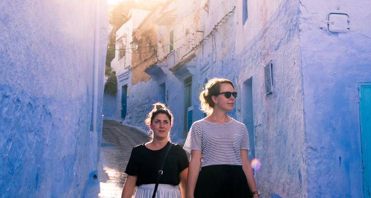 Zwei Frauen schlendern durch eine sonnenbeschienene blaue Gasse in Chefchaouen.